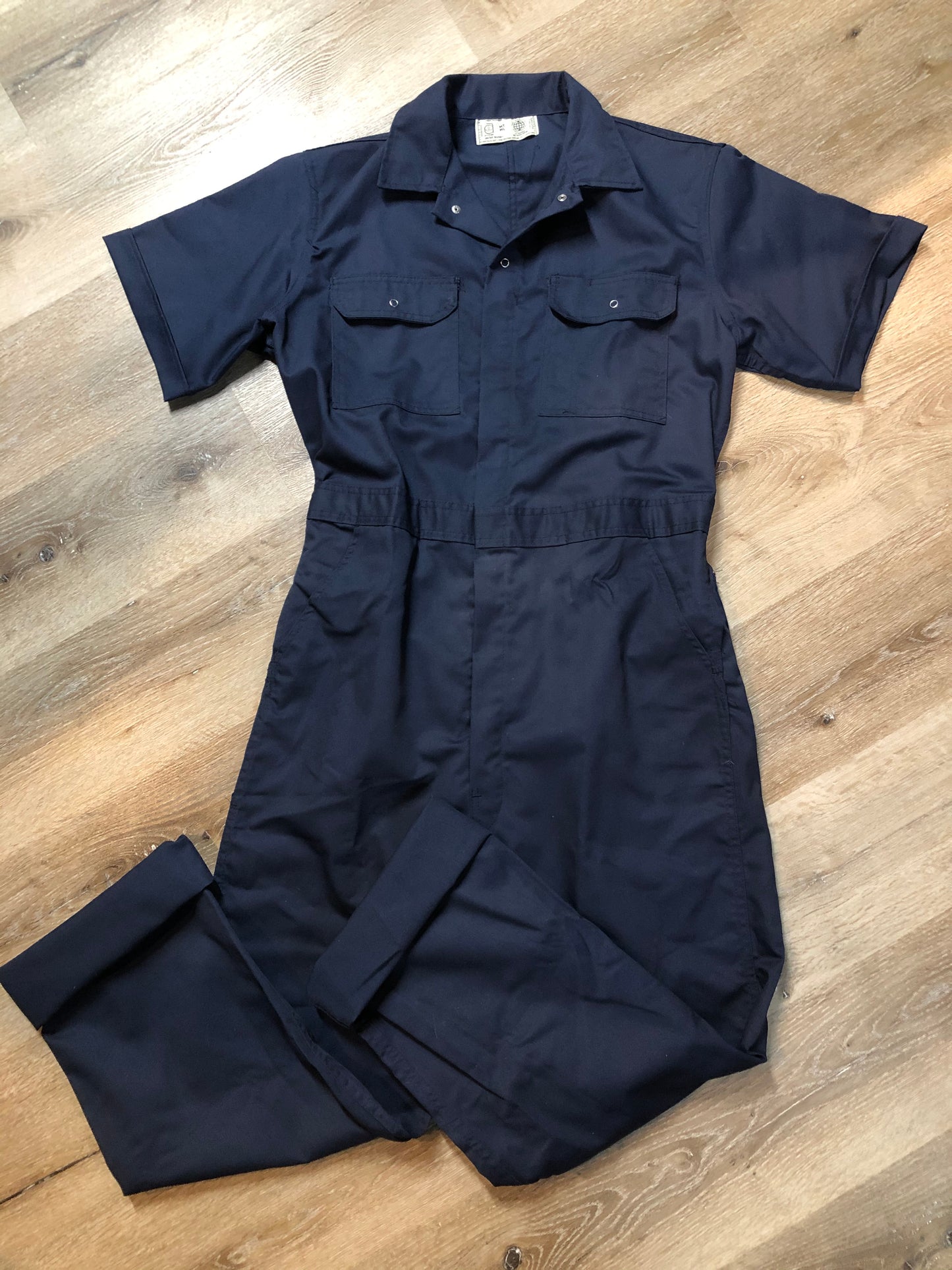 Kingspier Vintage - Vintage Deadstock Anchor Textiles short sleeve navy coveralls with snap closures, elastic waistband, flap pockets on the chest, slash pockets in the front and patch pockets in the back. Union made in Canada. Size medium/ large.