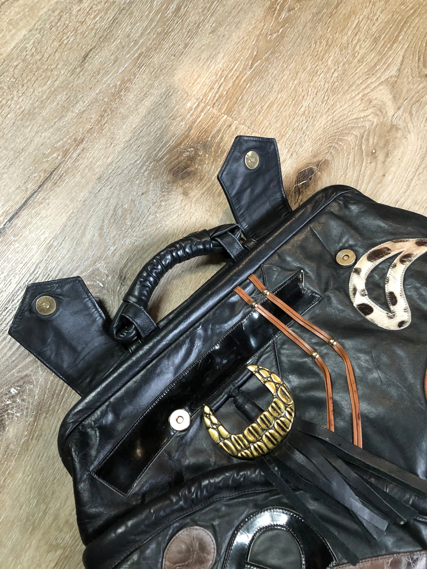 Kingspier Vintage - Upcycled leather bag with top handle, loops to attach a longer strap. (strap not included), snap closures, dinosaur and wooly mammoth design, a tassel and some other unique leather details.
Length - 18”
Width - 4”
Height - 13”
This bag is in great condition with some minor wear.