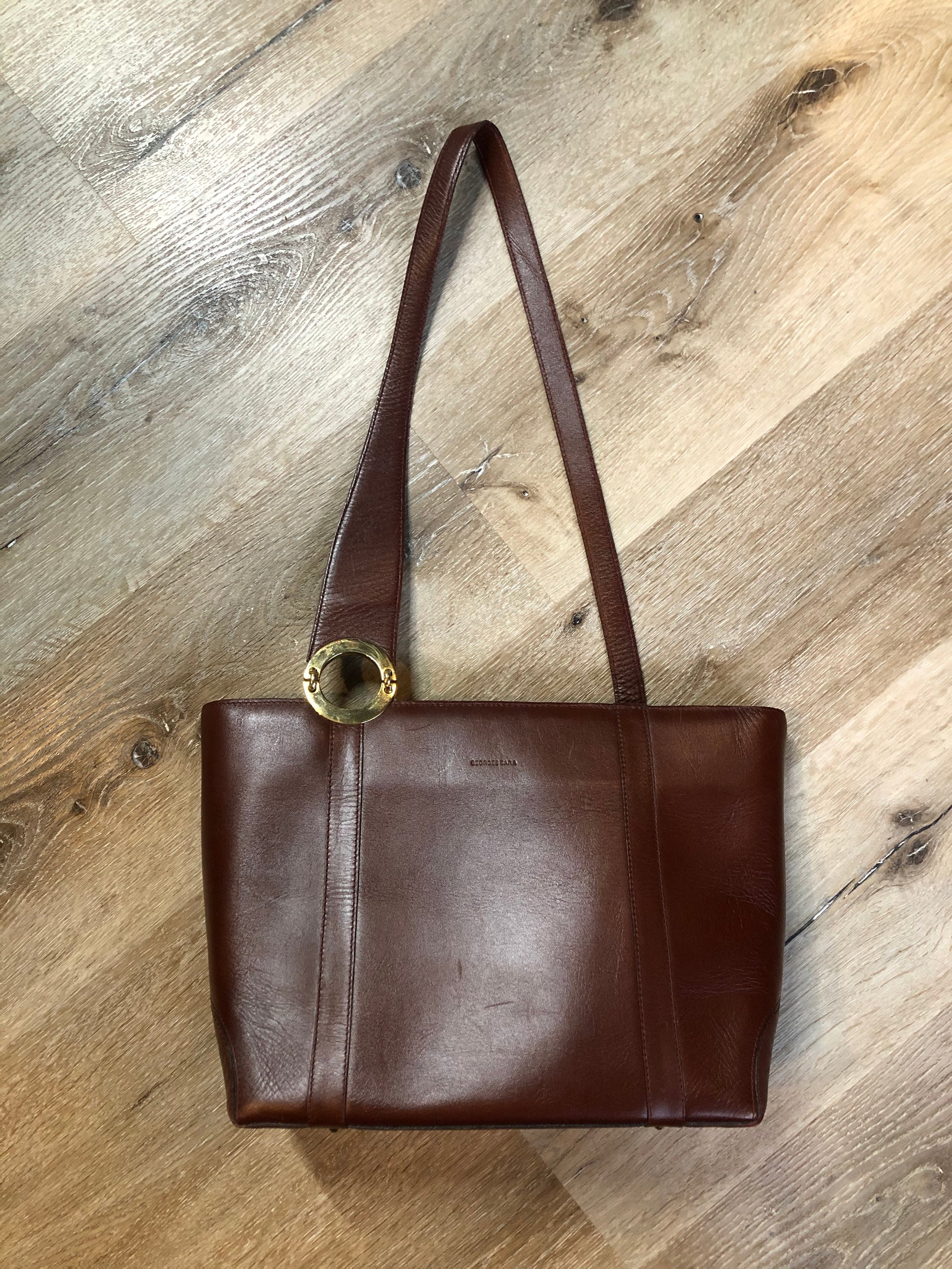 Kingspier Vintage - Georges Sara brown leather handbag with unique brass hardware, zipper top closure with three compartments inside. 
Length - 11.5”
Width - .5”
Height - 9”
Strap - 30”
This purse is in excellent condition.