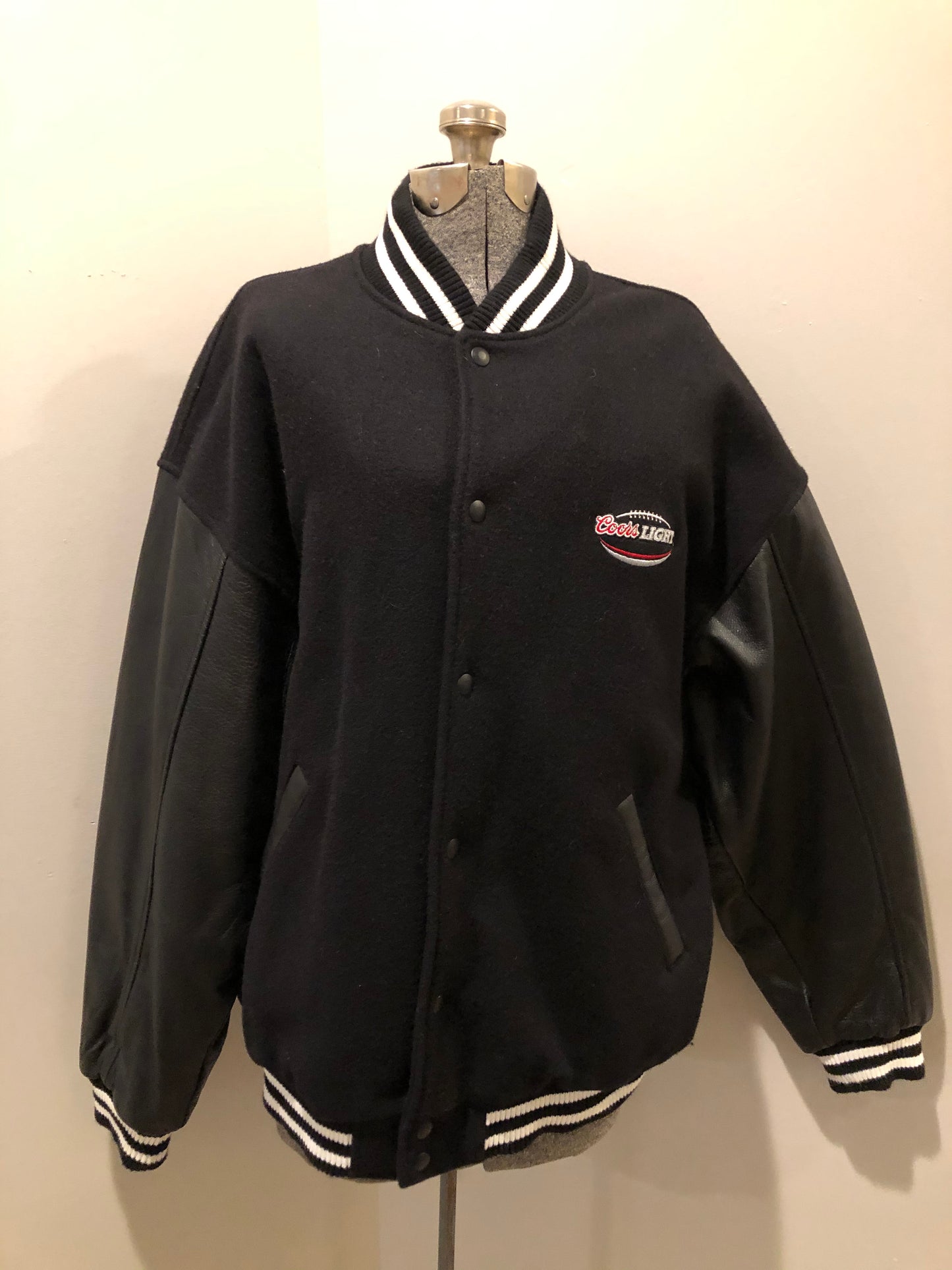 Kingspier Vintage - Coors Light black wool blend varsity jacket with black leather arms, knit trim, slash pockets, snap closure and a quilted lining. Men’s XL.