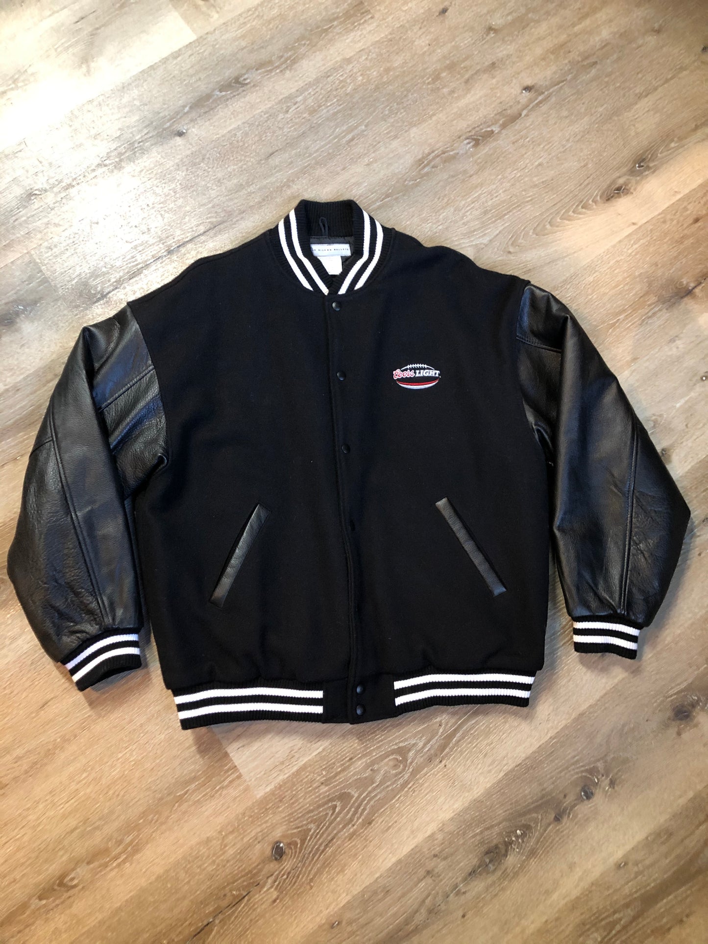 Kingspier Vintage - Coors Light black wool blend varsity jacket with black leather arms, knit trim, slash pockets, snap closure and a quilted lining. Men’s XL.