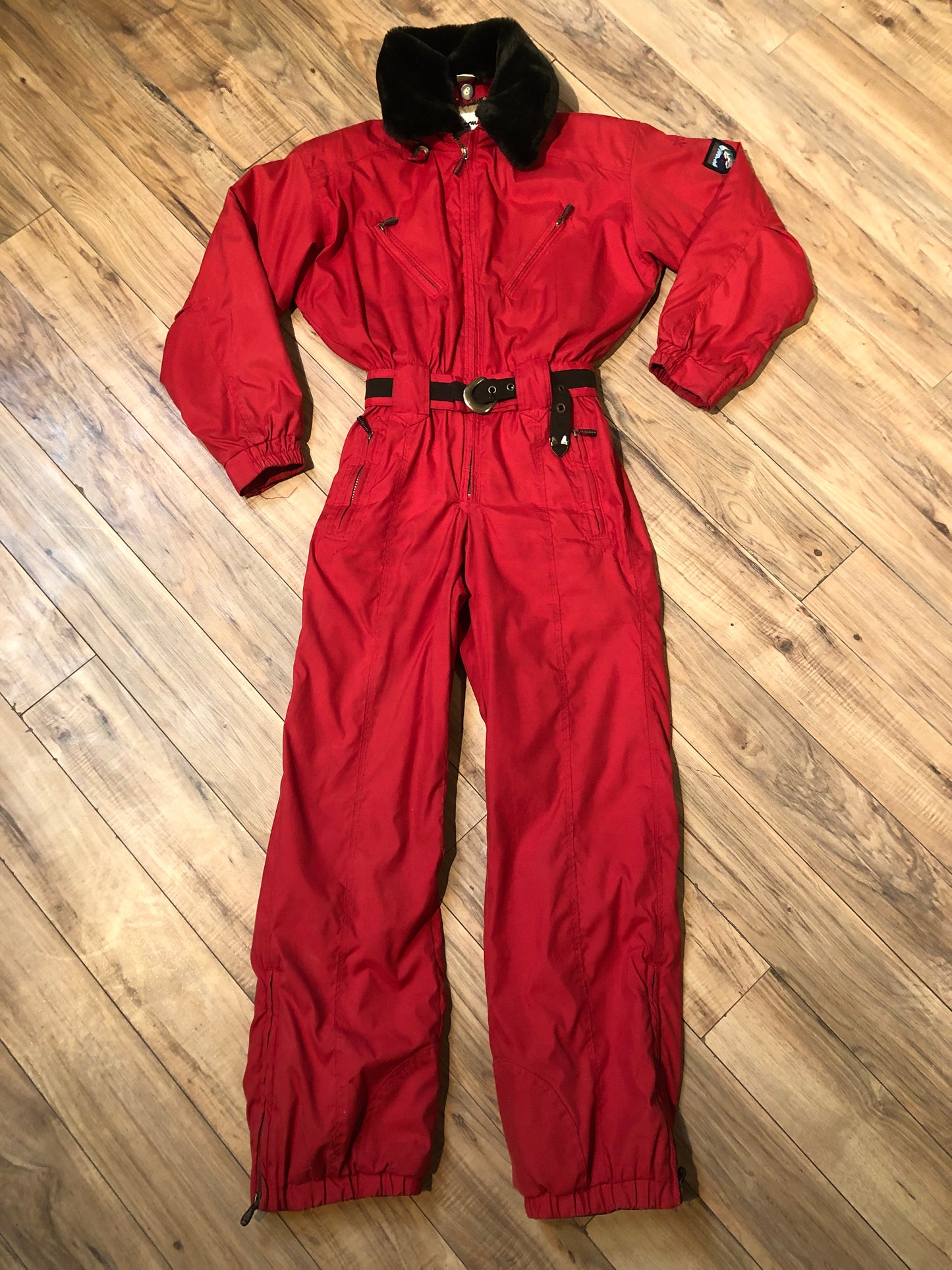 Kingspier Vintage - Vintage Obermeyer red one piece ski suit with suede belt, packable hood, quilted lining, zipper closure and multiple zip pockets.