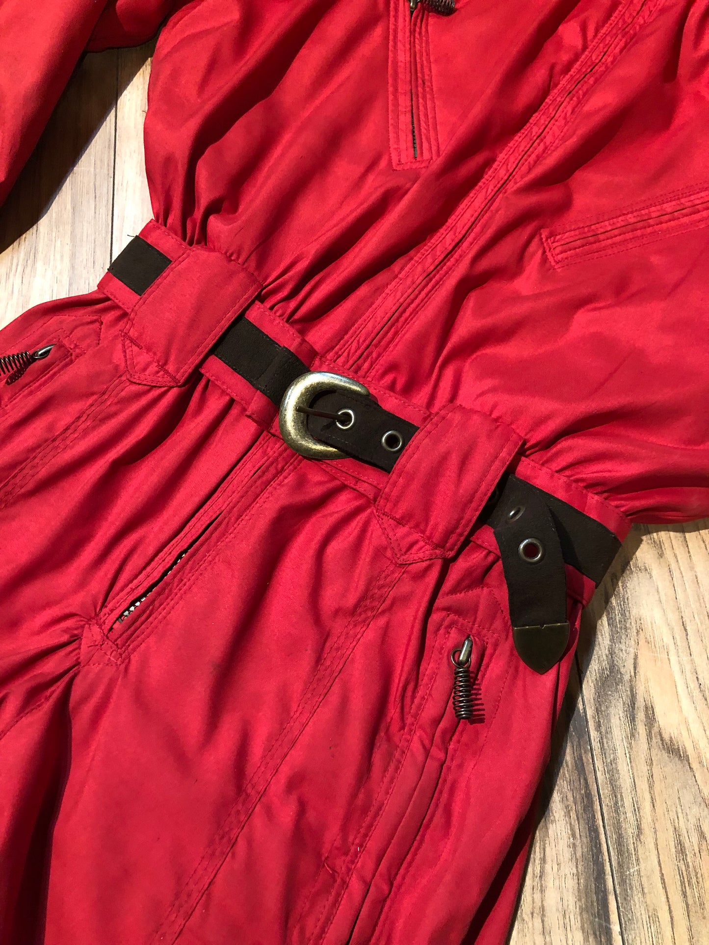 Kingspier Vintage - Vintage Obermeyer red one piece ski suit with suede belt, packable hood, quilted lining, zipper closure and multiple zip pockets.