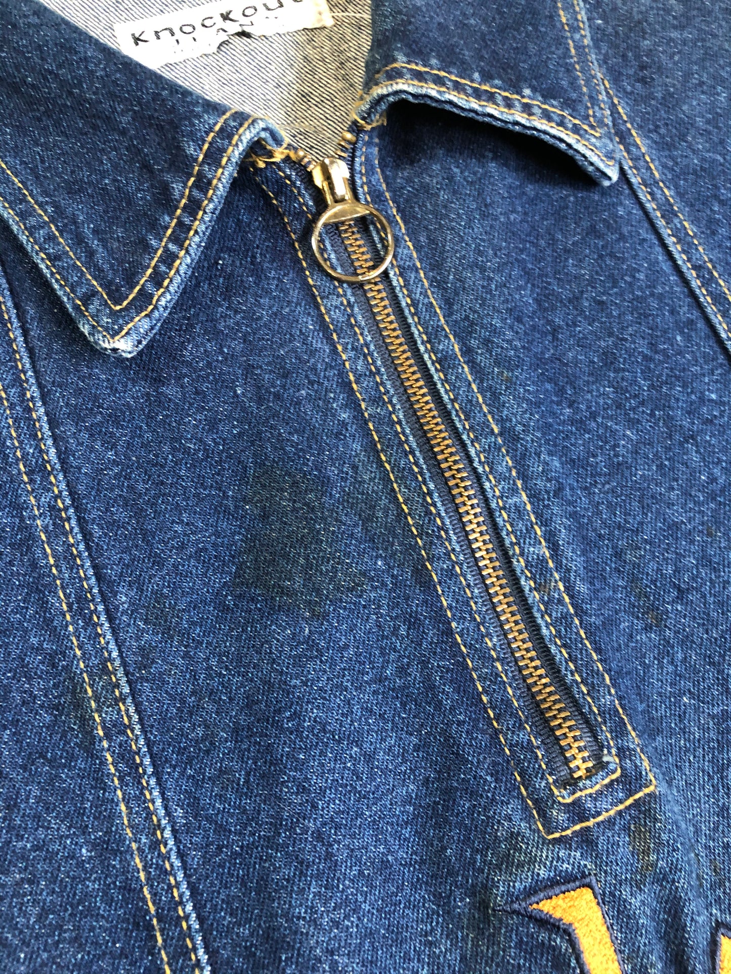 Kingspier Vintage - Vintage Knockout Jeans pullover denim jacket in a medium wash with quarter zip closure, embroidered logo on the front, knit cuffs, slash pockets, one patch pocket on the chest and a leather patch on the back. Size Xl. Made in USA