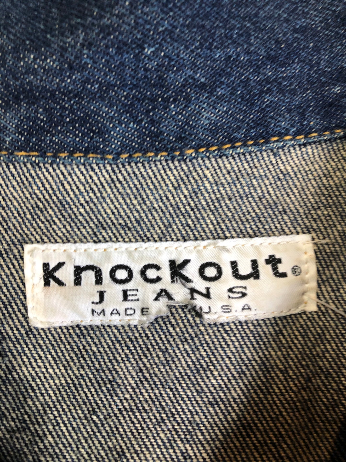 Kingspier Vintage - Vintage Knockout Jeans pullover denim jacket in a medium wash with quarter zip closure, embroidered logo on the front, knit cuffs, slash pockets, one patch pocket on the chest and a leather patch on the back. Size Xl. Made in USA