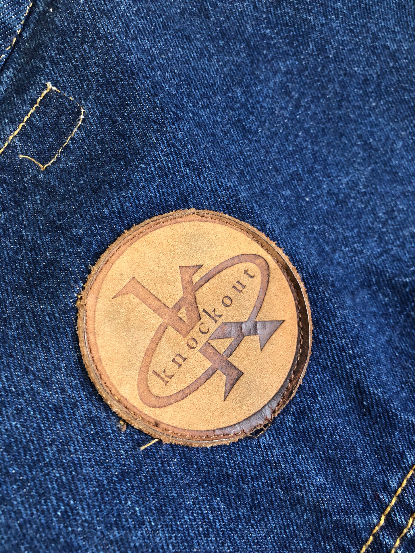 Kingspier Vintage - Vintage Knockout Jeans pullover denim jacket in a medium wash with quarter zip closure, embroidered logo on the front, knit cuffs, slash pockets, one patch pocket on the chest and a leather patch on the back. Size Xl. Made in USA
