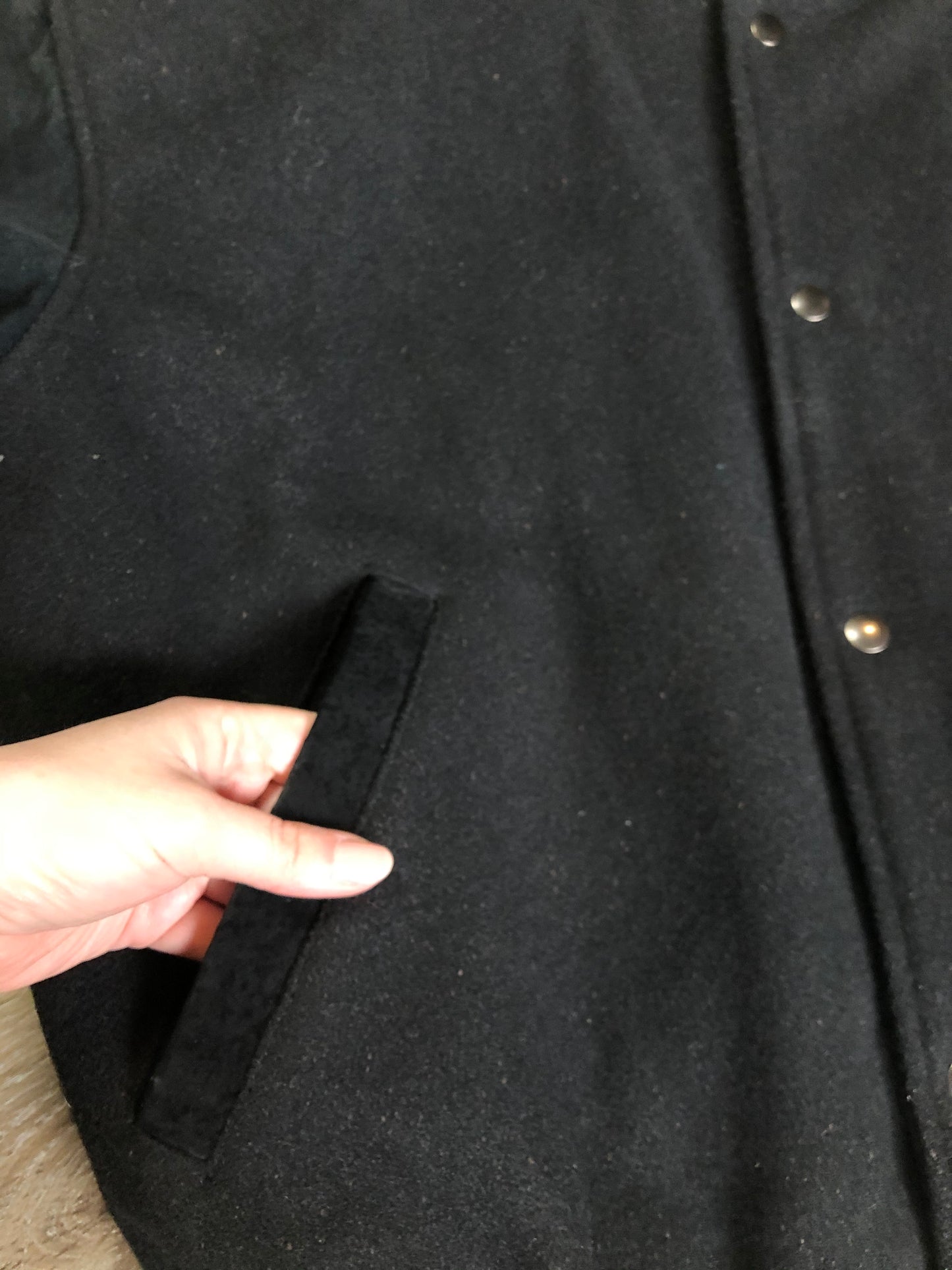Kingspier Vintage - Vintage Levi’s black wool blend varsity jacket with Levi’s logo embroidered on the chest, “Levi’s Blue Jeans, Factory Made” with a large illustration of a factory across the back, micro suede sleeves, snap closures, slash pockets, polyester lining, one inside pocket and knit trim. Made in Canada. Size medium.