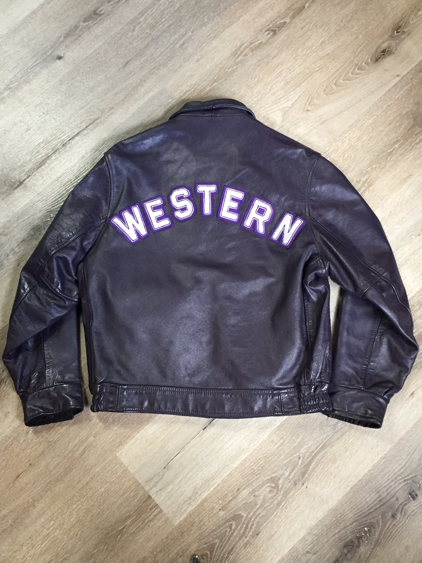 Kingspier Vintage - Western University leather varsity jacket in deep purple with slash pockets and snap closures, emblem embroidered on the chest and “Western” written across the back.