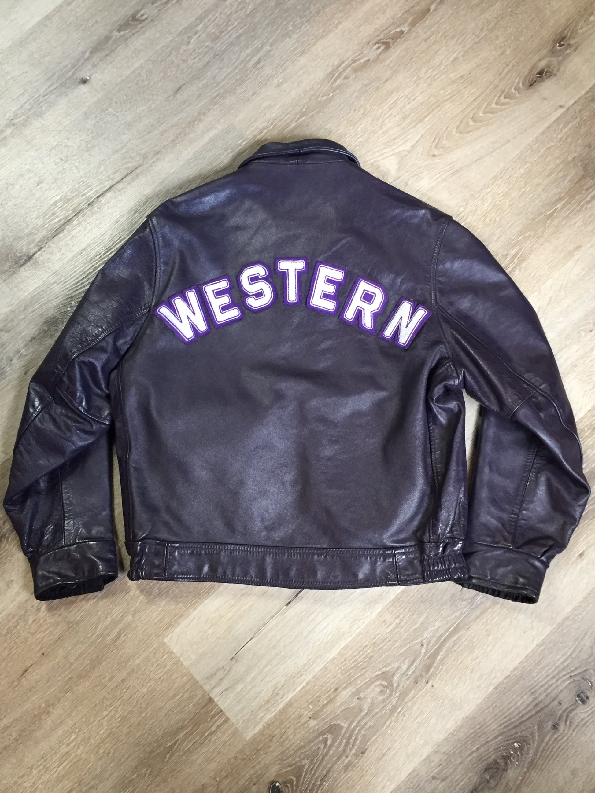 Kingspier Vintage - Western University leather varsity jacket in deep purple with slash pockets and snap closures, emblem embroidered on the chest and “Western” written across the back.