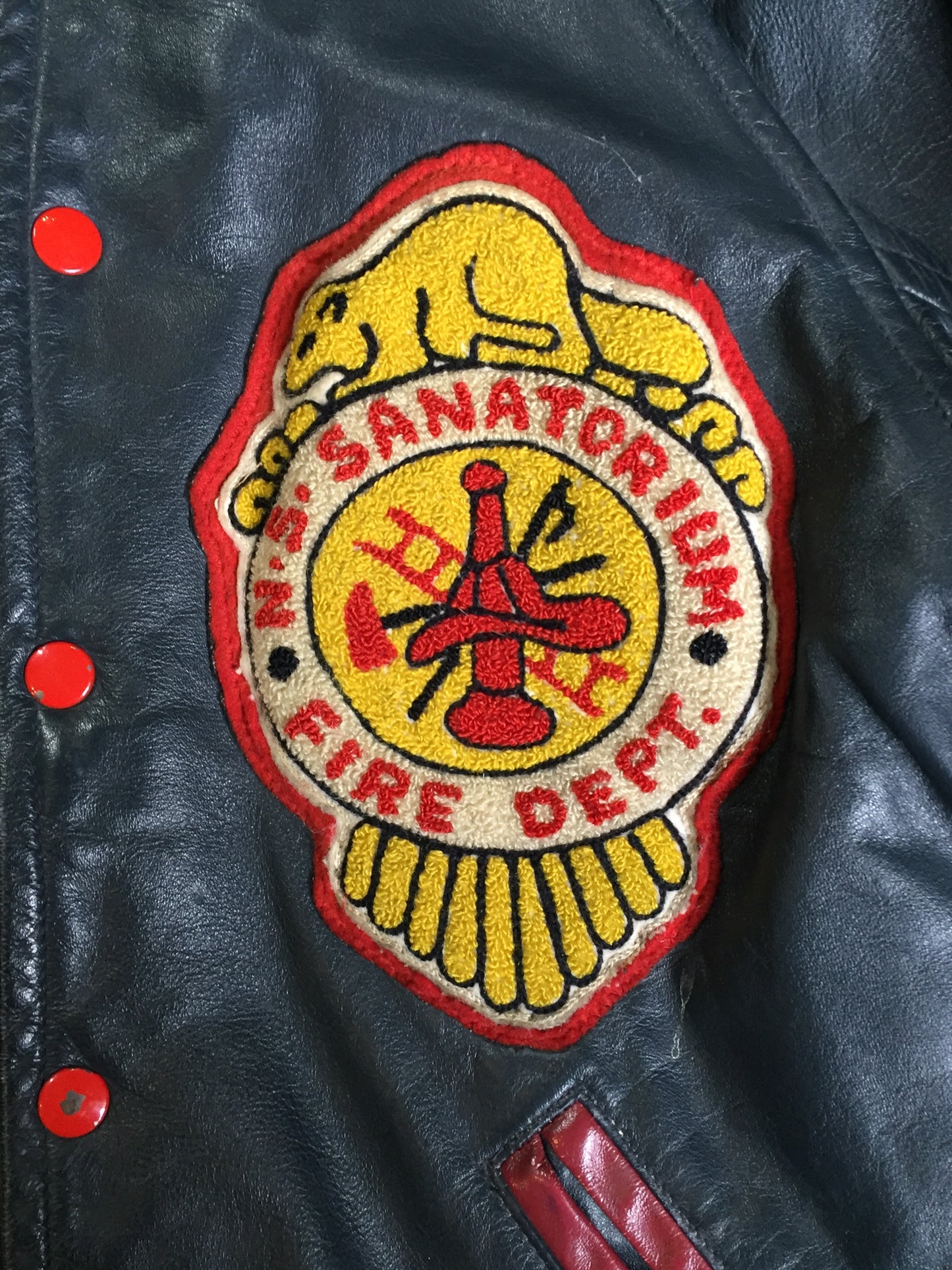 Kingspier Vintage - NS Sanitorium Fire Department green leather varsity jacket with red details, snap closures, slash pockets, embroidered emblem on the chest, embroidered monogram on the arm and shearling lining.