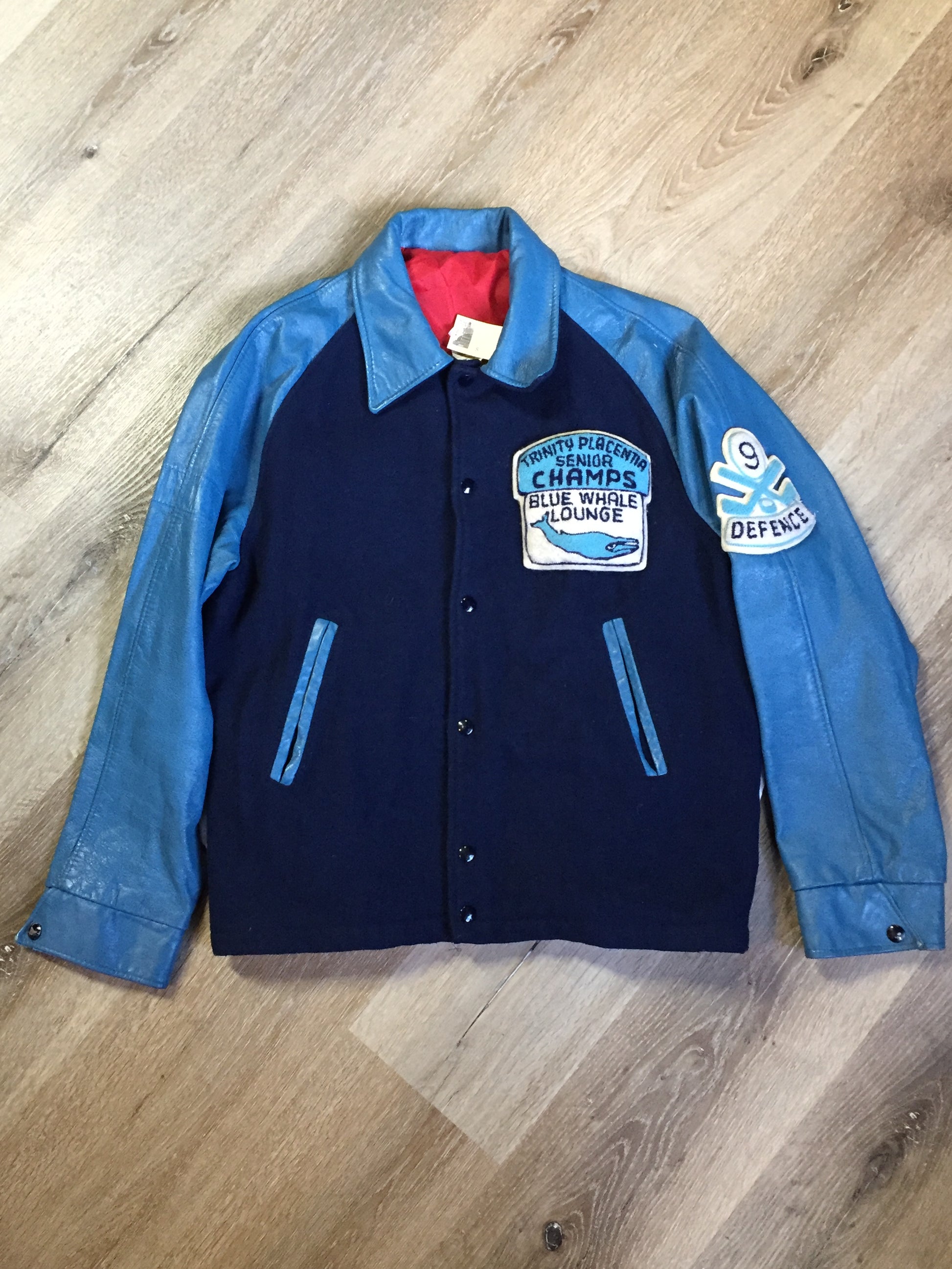 Kingspier Vintage - Trinity Placentia Senior Champs “Blue Whale Lounge “ blue varsity jacket with snap closures, slash pockets, embroidered emblem on chest and arm, “whalers” written across the back and a red lining. Size 44.