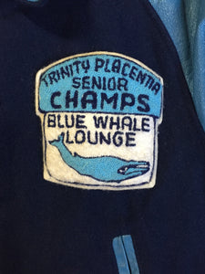 Kingspier Vintage - Trinity Placentia Senior Champs “Blue Whale Lounge “ blue varsity jacket with snap closures, slash pockets, embroidered emblem on chest and arm, “whalers” written across the back and a red lining. Size 44.