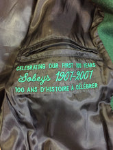 Load image into Gallery viewer, Kingspier Vintage - Roots “Sobey’s Centenary Anniversary” ’07 varsity jacket in green and white with snap closures, slash pockets, knit trim, embroidered “100” emblem on the chest and “07” on the arm.
