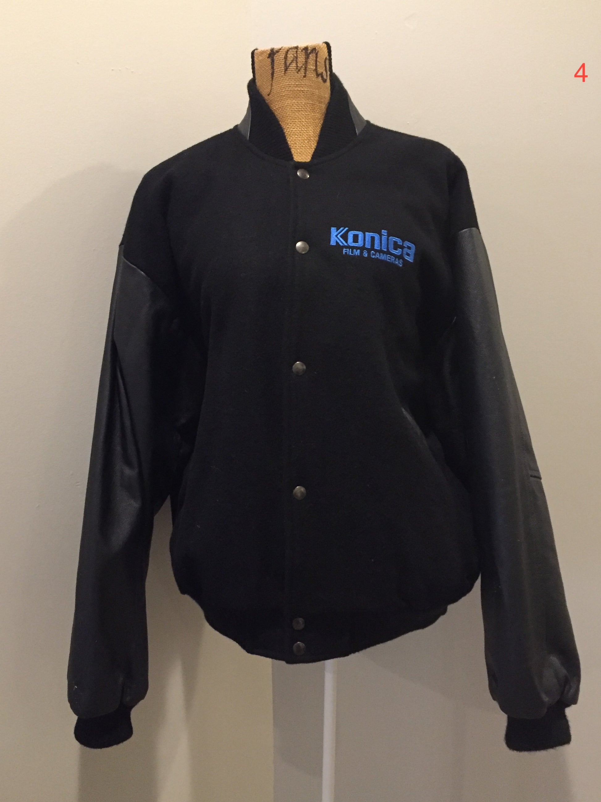 Kingspier Vintage - Konica “film and Cameras” wool and leather varsity jacket in black with snap closures, slash pockets, inside pocket and “get ready” written across the back with a race car illustration. Size large.