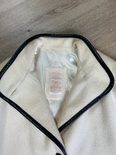 Load image into Gallery viewer, Kingspier Vintage - Genuine Hudson Bay Company 100% virgin wool coat in white with black leather trim, front pockets, flat black buttons and a unique mandarin collar with cape style detail around shoulders. Contains a Hudson’s Bay seal of quality tag. Made in Canada.
