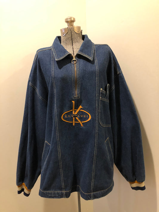 Kingspier Vintage - Vintage Knockout Jeans pullover denim jacket in a medium wash with quarter zip closure, embroidered logo on the front, knit cuffs, slash pockets, one patch pocket on the chest and a leather patch on the back. Size Xl. Made in USA