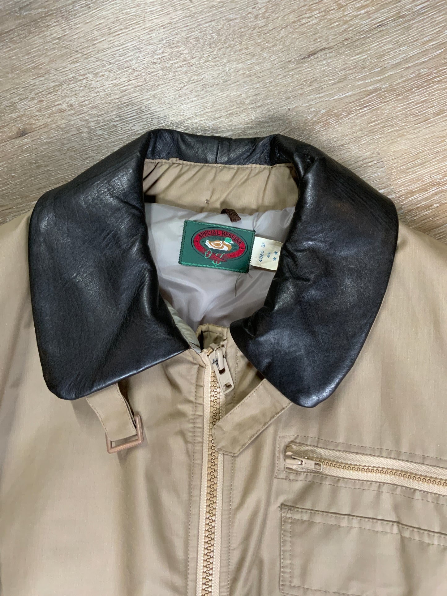 Kingspier Vintage - Special Reserve hunting jacket in beige with brown leather collar featuring a strap to keep your collar in place, zipper, three flap pockets and one zip pocket. Knit inside cuffs. lined for cooler weather with drawstring at waist. Made in Canada. Size 44. 