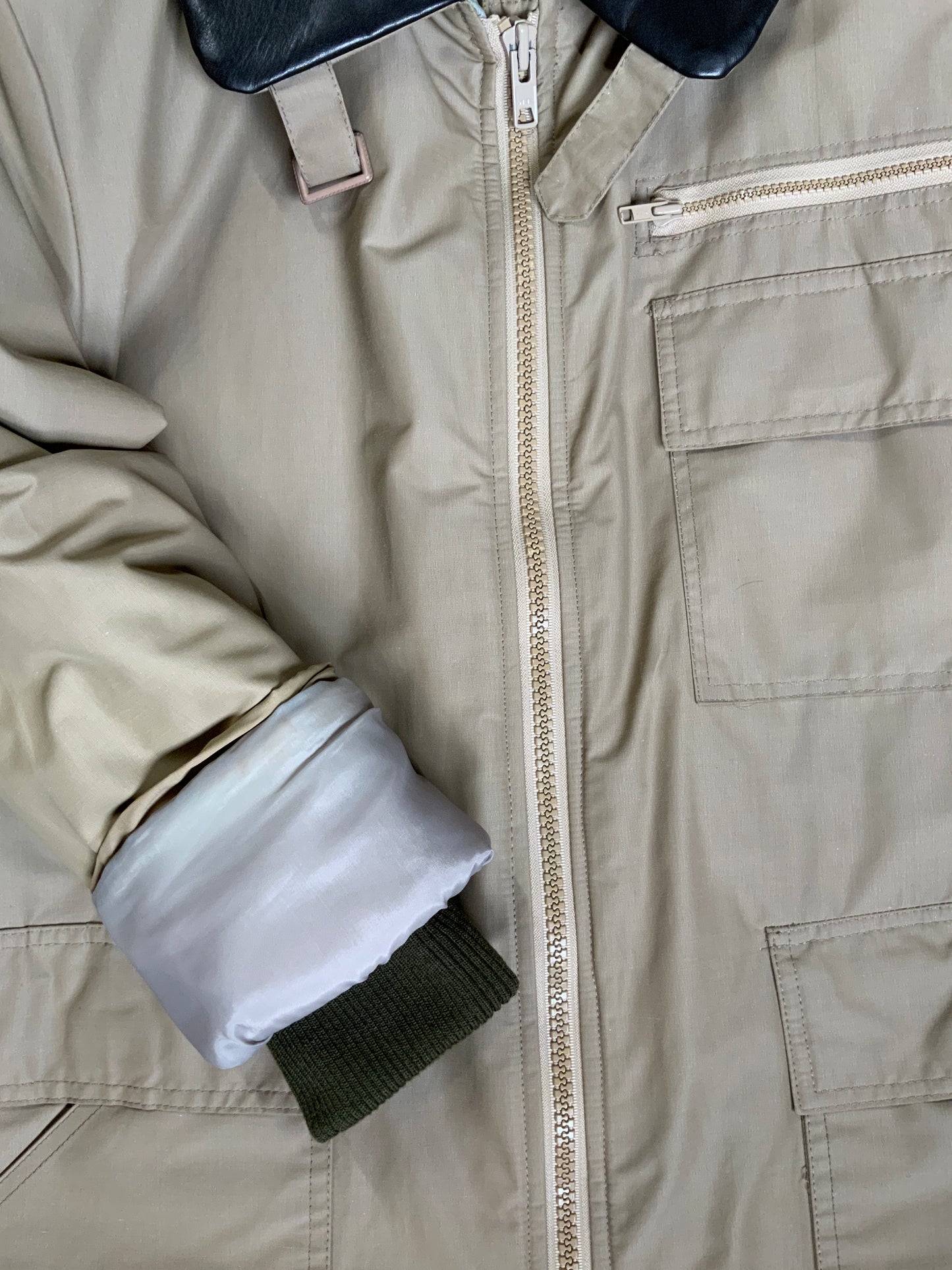 Kingspier Vintage - Special Reserve hunting jacket in beige with brown leather collar featuring a strap to keep your collar in place, zipper, three flap pockets and one zip pocket. Knit inside cuffs. lined for cooler weather with drawstring at waist. Made in Canada. Size 44. 