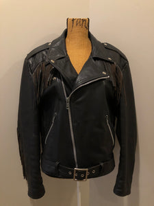 Kingspier Vintage - Action black leather motorcycle jacket with fringe detail and belt at waist. Zipper closure and zip slash pockets, quilted lining with inside pocket. Made in Canada. Size 40. 