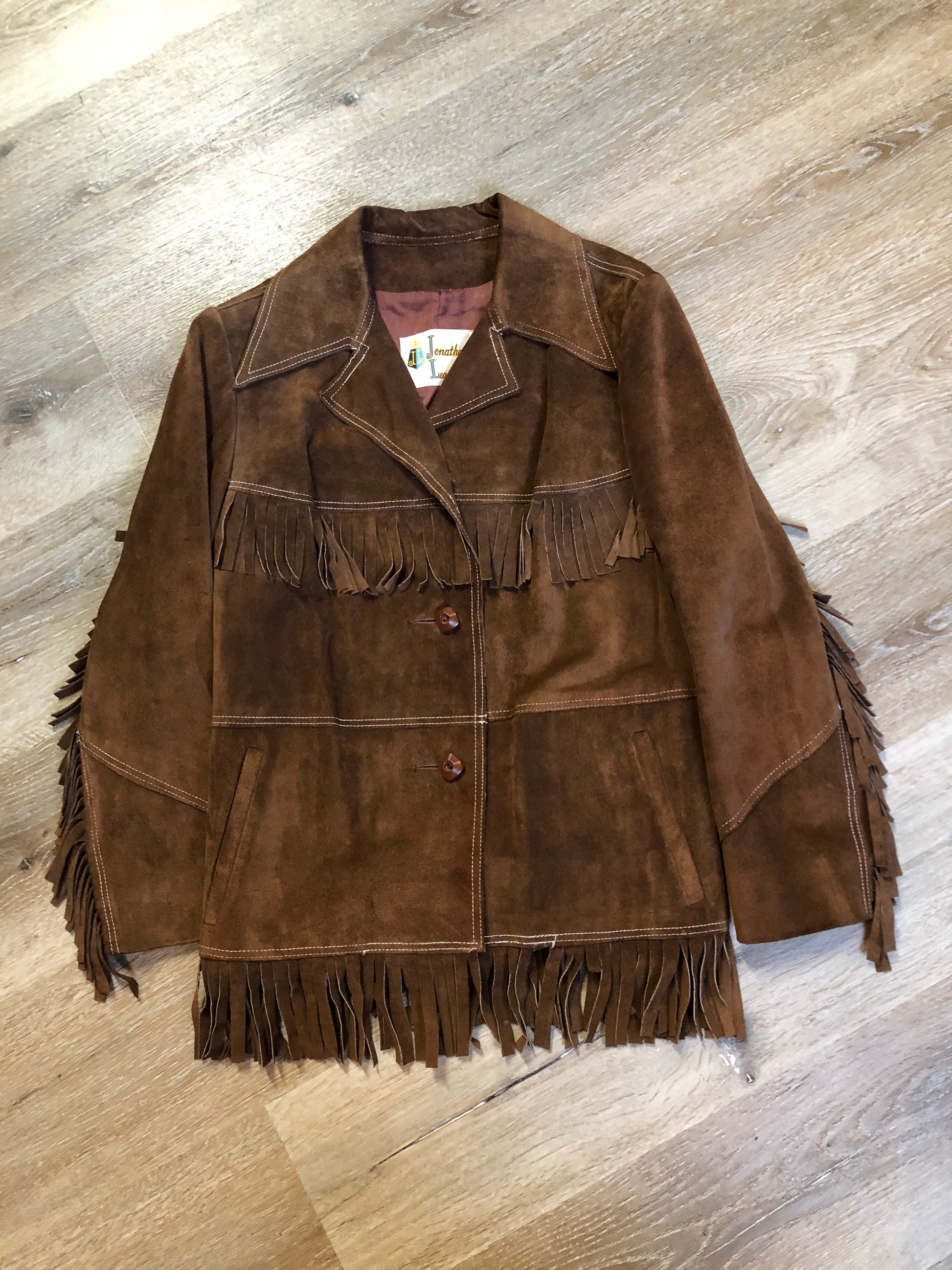 Kingspier Vintage - Jonathan Legault brown suede western style jacket with fringe details, belt in the back, button closures and slash pockets. 