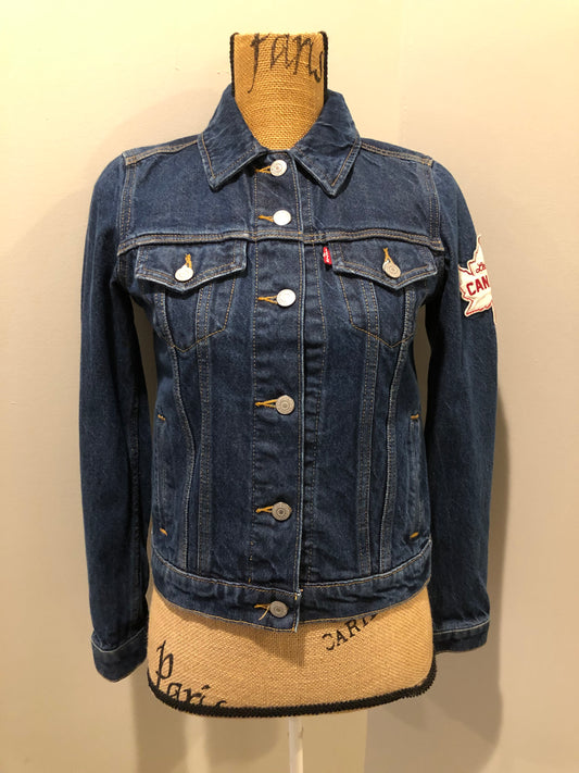 Kingspier Vintage - Levi’s Original Trucker Jacket in a medium wash denim with Canada leaf patch on the left shoulder, button closures, two vertical pockets and two flap pockets on the chest. Size XS.