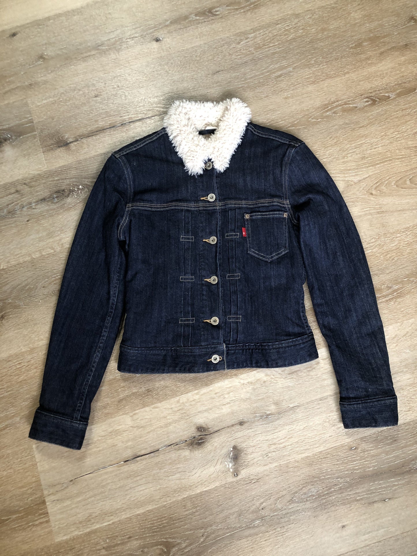 Kingspier Vintage - Levi’s Sherpa style denim jacket in a dark wash with stretch, pleats running down the front, faux fur lining and quilted lining in both arms, button closures and one patch pocket. Size XS.