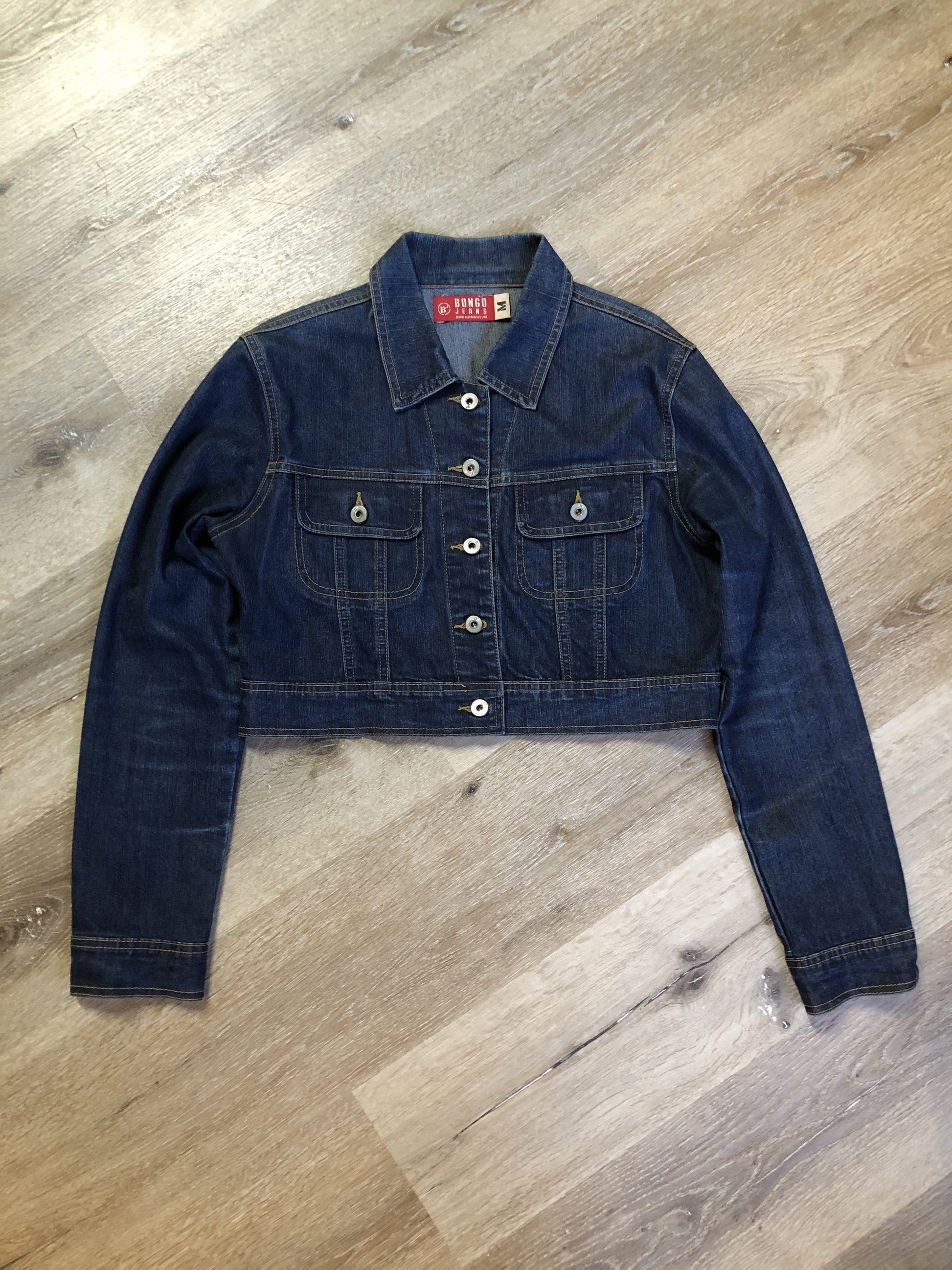 Kingspier Vintage - Bongo Jeans cropped denim jacket in a dark wash with whiskering on the arms, button closures and flap pockets on the chest. Size medium.