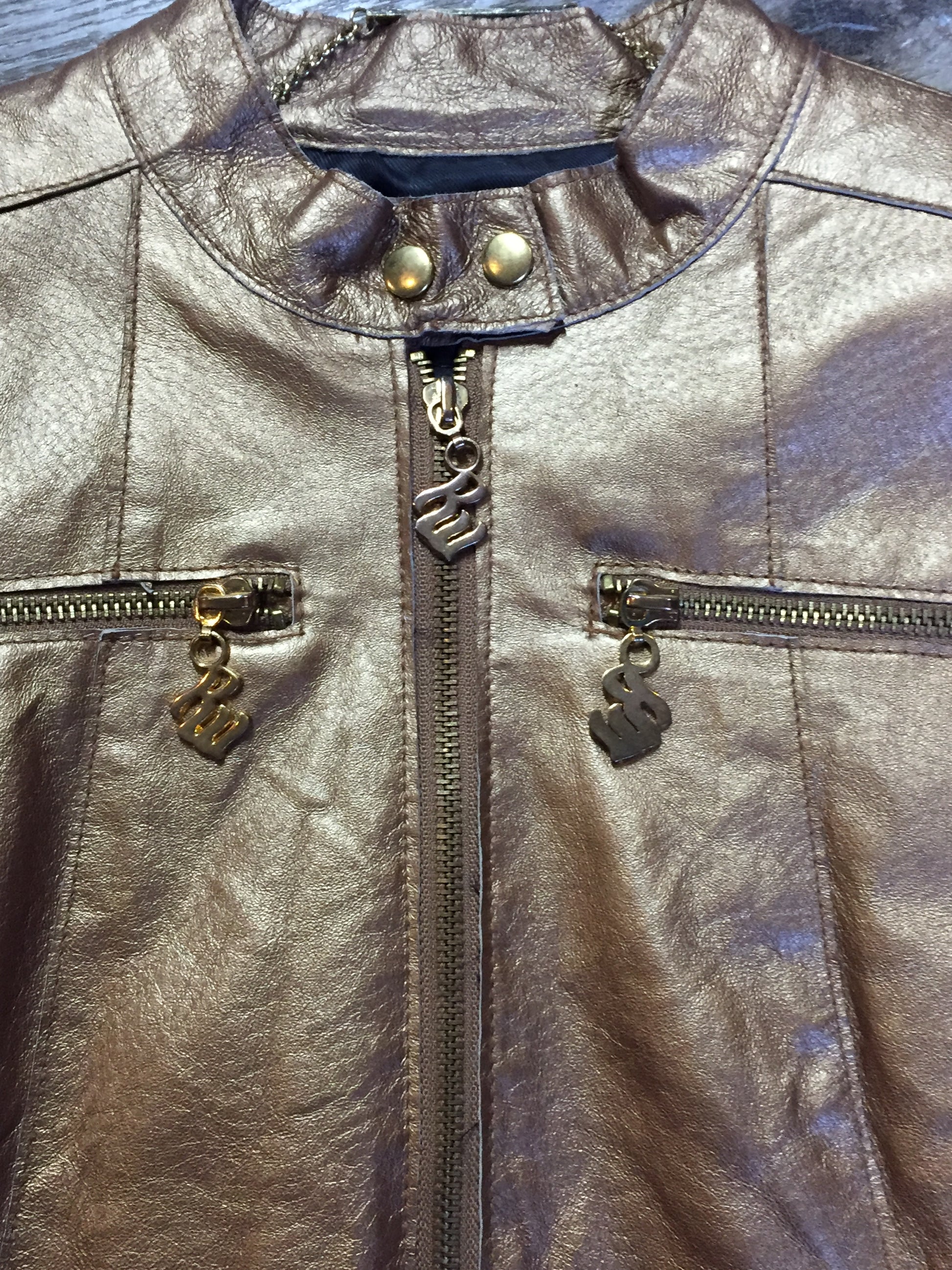 Kingspier Vintage - Rocawear metallic gold leather moto jacket with “RW” detail zippers, chain lace-up detail on sides and “ROCAWEAR” written in chain across the back. There is a front zipper, two horizontal zip pockets on the chest, two snap closures on the stand up collar and a pocket on the inside. Size small.