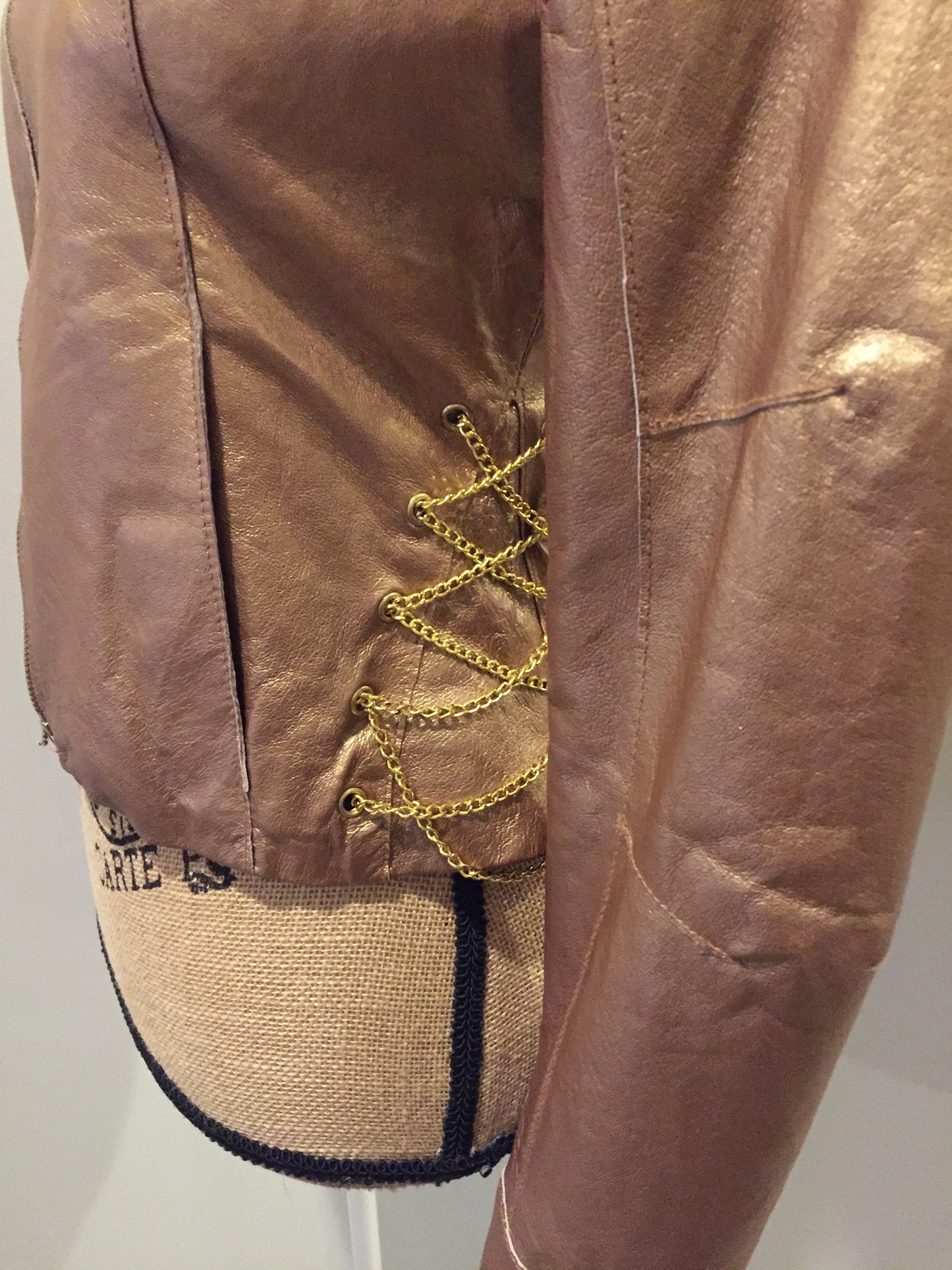 Kingspier Vintage - Rocawear metallic gold leather moto jacket with “RW” detail zippers, chain lace-up detail on sides and “ROCAWEAR” written in chain across the back. There is a front zipper, two horizontal zip pockets on the chest, two snap closures on the stand up collar and a pocket on the inside. Size small.