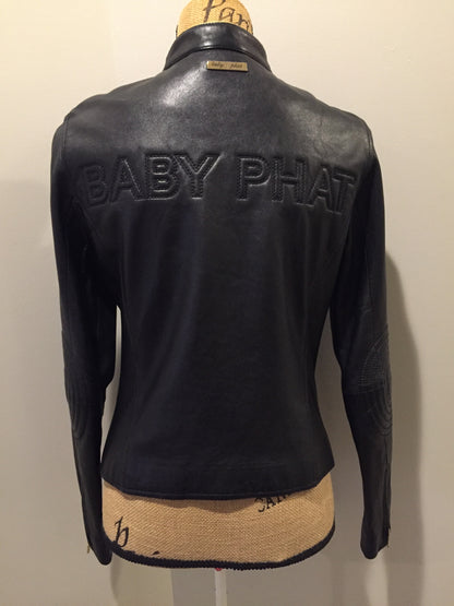 Kingspier Vintage - Baby Phat black leather moto jacket with gold piping and “Baby Phat” embroidered on the chest, front zipper and two vertical zip pockets. A pattern is stitched into the elbows and “Baby Phat” is stitched across the back. Size small.