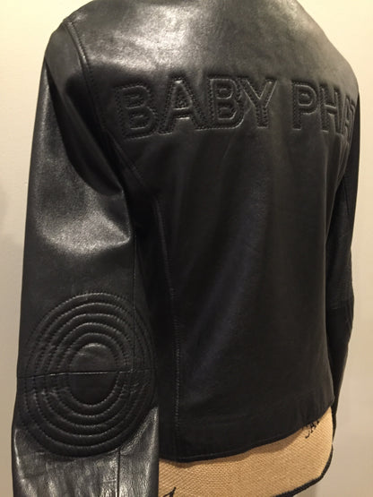 Kingspier Vintage - Baby Phat black leather moto jacket with gold piping and “Baby Phat” embroidered on the chest, front zipper and two vertical zip pockets. A pattern is stitched into the elbows and “Baby Phat” is stitched across the back. Size small.