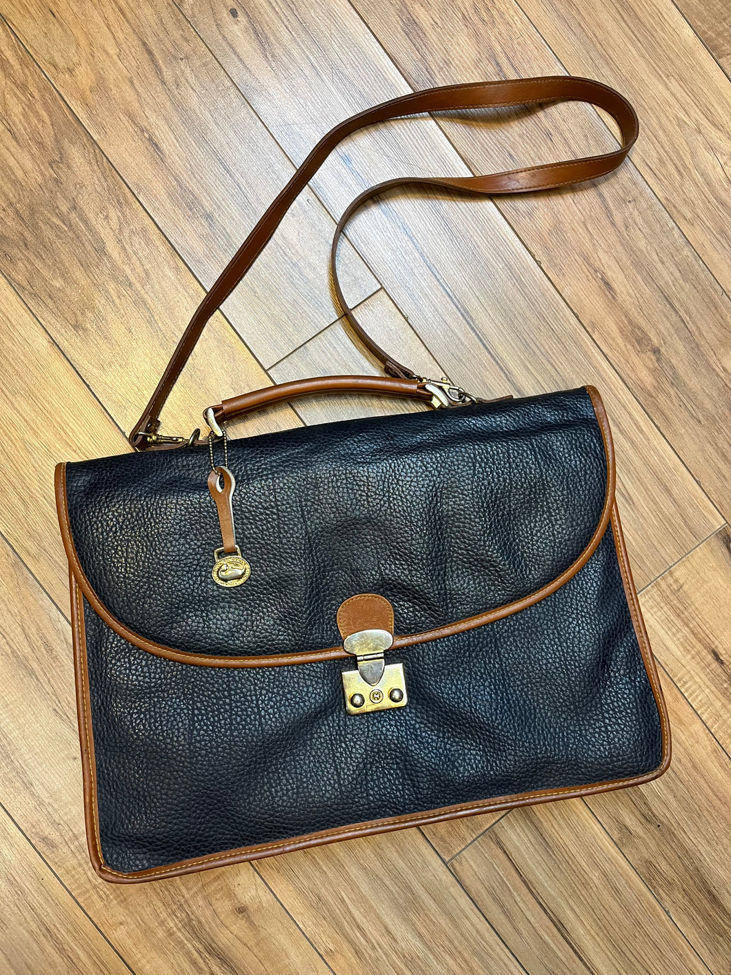 Dooney and Burke all weather leather briefcase in navy with top handle, shoulder strap and brass hardware.