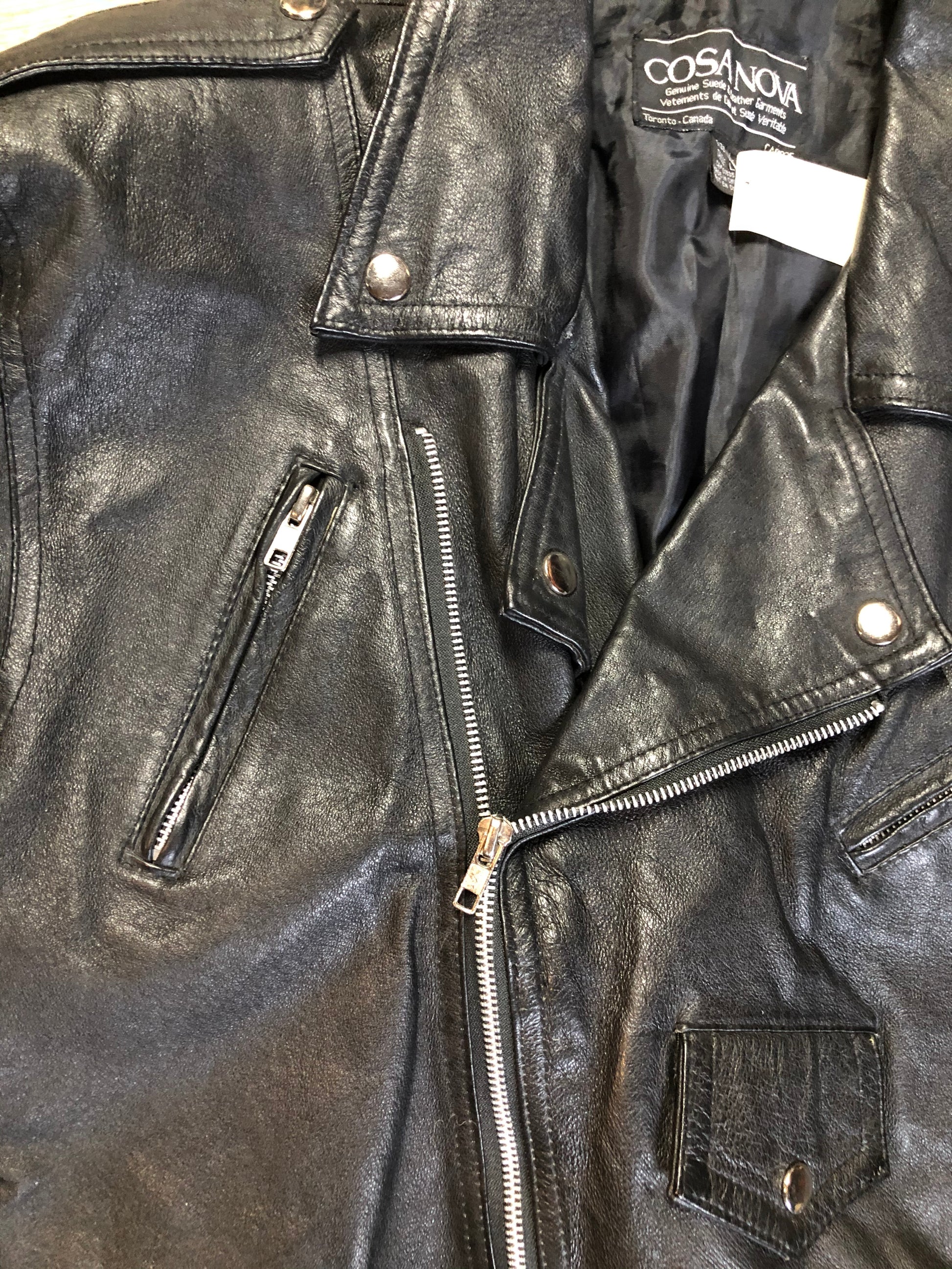 Kingspier Vintage - Cosa Nova black leather motorcycle jacket with two slash pockets, one flap pocket and a belt at the waist. Made in Canada. Size large.