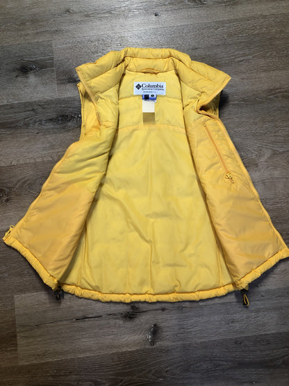 Kingspier Vintage - Columbia down filled puffer vest in yellow with zipper closure, vertical zip pockets, inside pocket and drawstring at the bottom hem. Size medium.