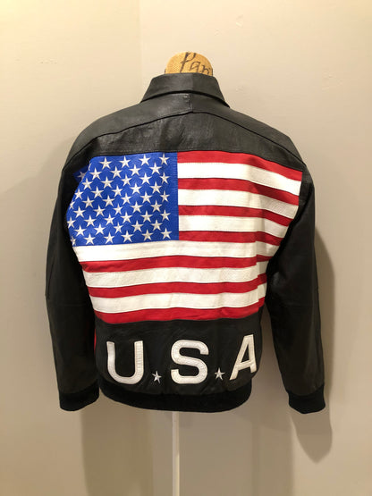 Kingspier Vintage - Two Plus Two black leather jacket with red and white details, large American flag on the back with USA written across the bottom. Slash pockets zipper closure, one inside pocket, nylon lining, knit cuffs and trim.