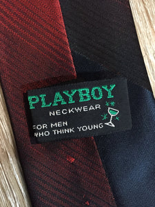 Kingspier Vintage - Playboy tie with navy, red, yellow and green design. Fibres unknown. 

Length: 57.5” 
Width: 2.5” 

This tie is in excellent condition.