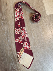 Kingspier Vintage - Van Heussen de Luxe in burgundy, red, cream and brown design on a subtle checkerboard background. Fibres unknown.

Length: 53” 
Width: 4”

This tie is in excellent condition.