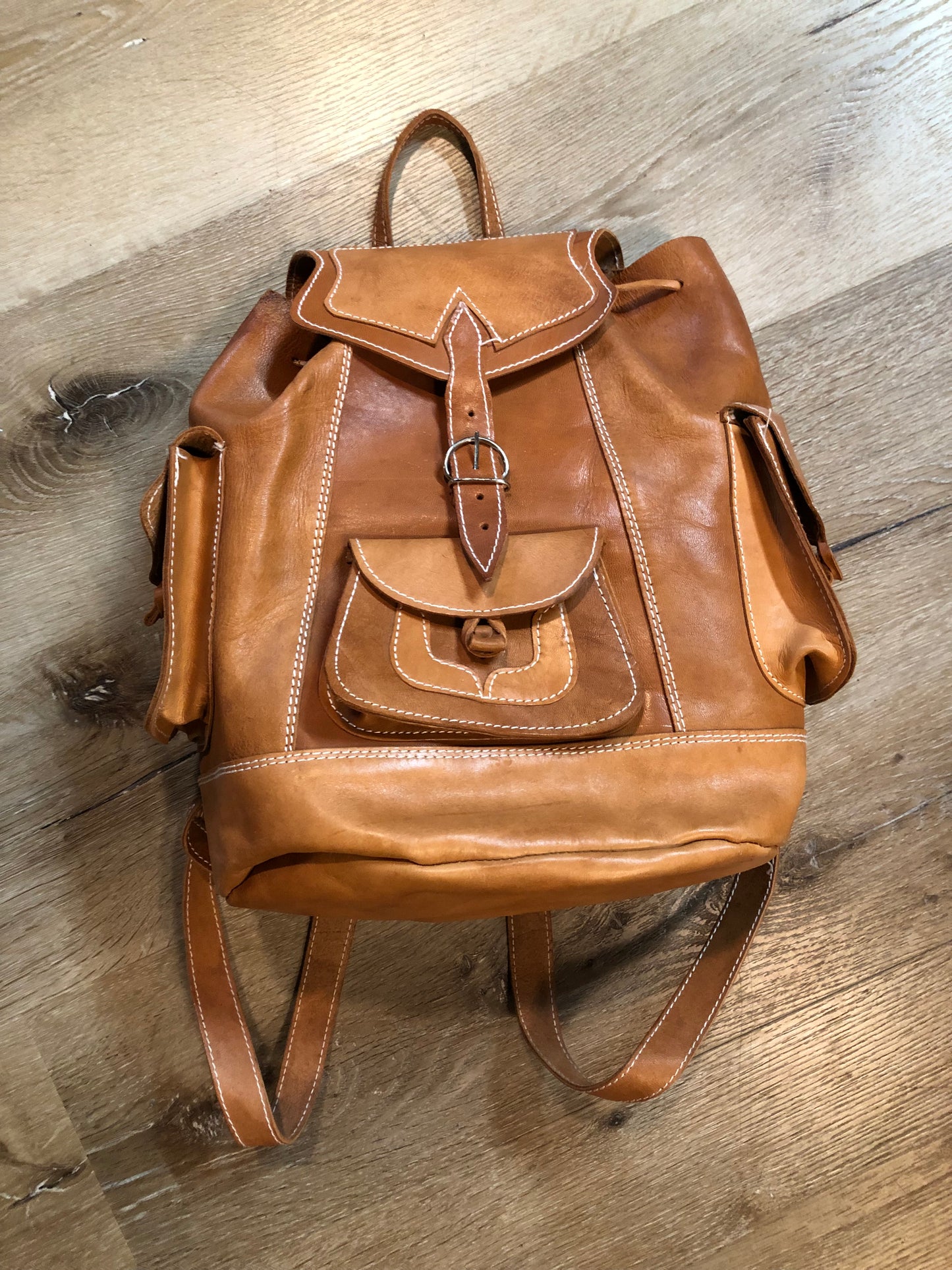 Vintage full grain leather backpack in light brown with top carry handle, flap closure, interior drawstring, three exterior compartments and adjustable shoulder straps Kingspier Vintage