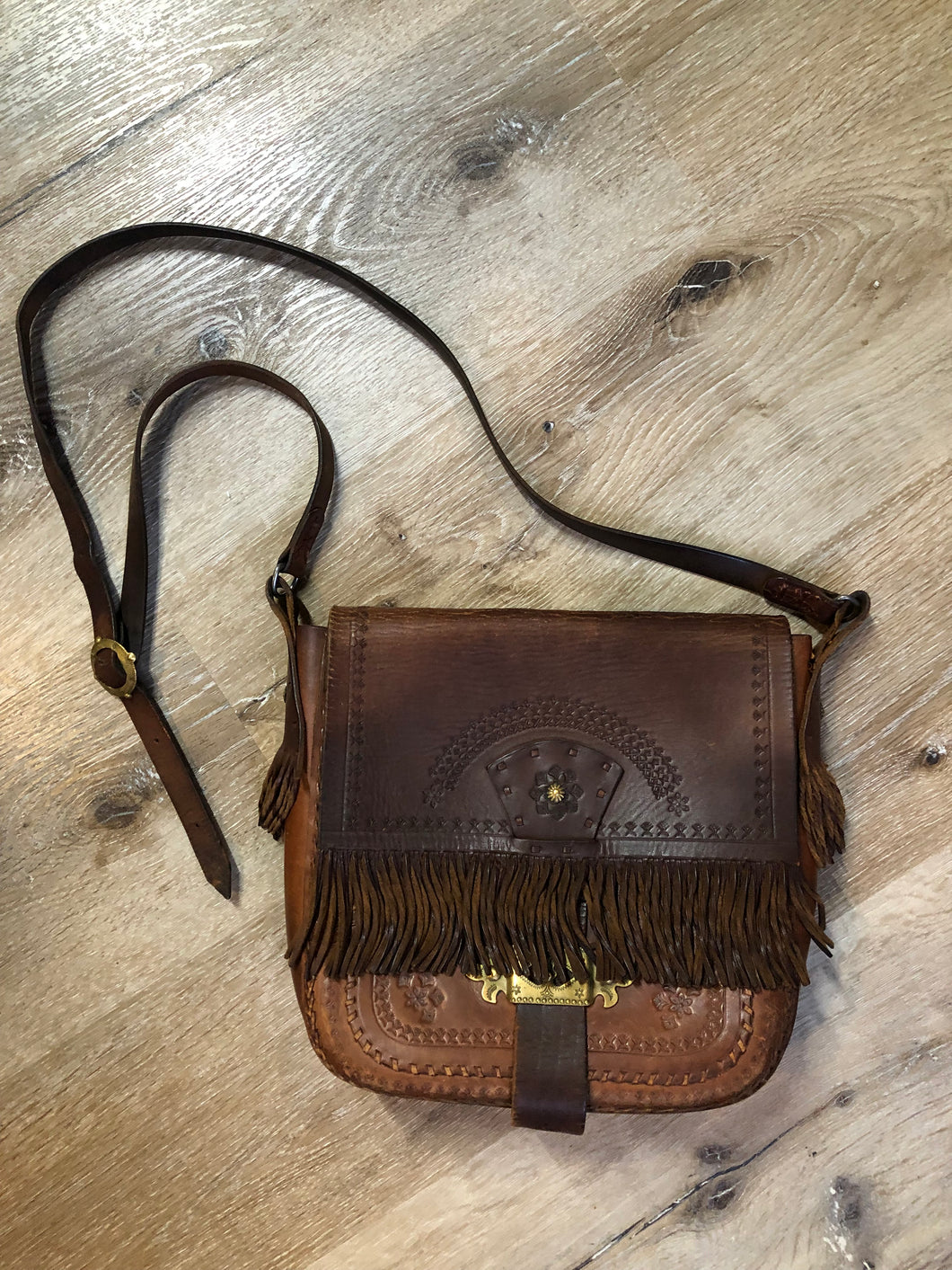 Vintage full grain brown leather crossbody bag with leather fringe, hand tooled designs, brass hardware, flap closure, two interior compartments and adjustable shoulder strap.  Bag is scented with patchouli - Kingspier Vintage