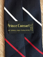 Load image into Gallery viewer, Kingspier Vintage - Prince Consort 100% polyester tie in navy with white and red stripes and a small jet illustration at the bottom center of the tie. Made for the U.S. airforce.
 
Length: 58.25” 
Width: 3” 

This tie is in excellent condition.
