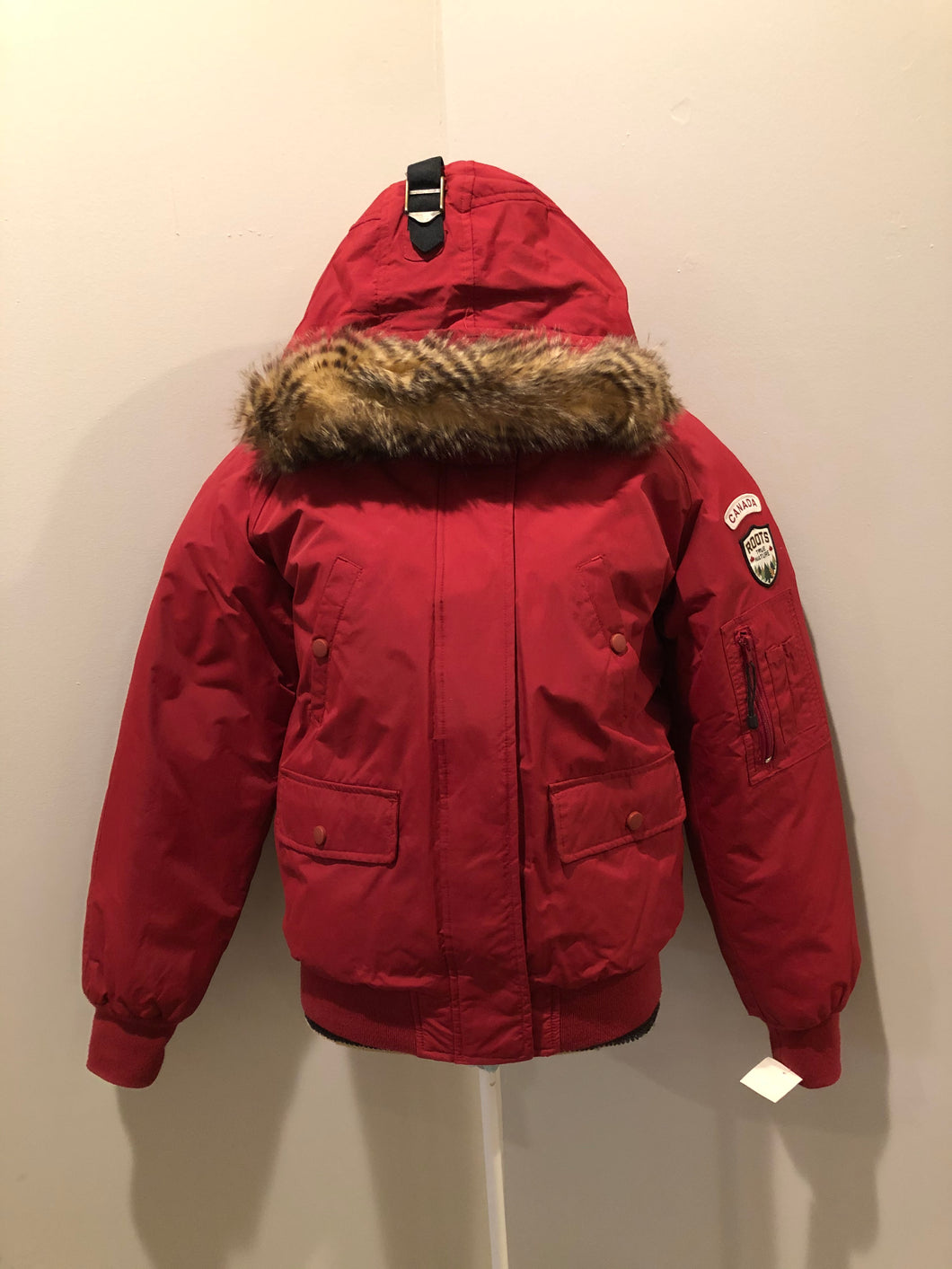 Kingspier Vintage - Roots down-filled bomber jacket in red with faux fur trimmed hood, zipper closure, flap pockets and slash pockets, “Stay Warm Eh” written on the inside pocket. Size medium.