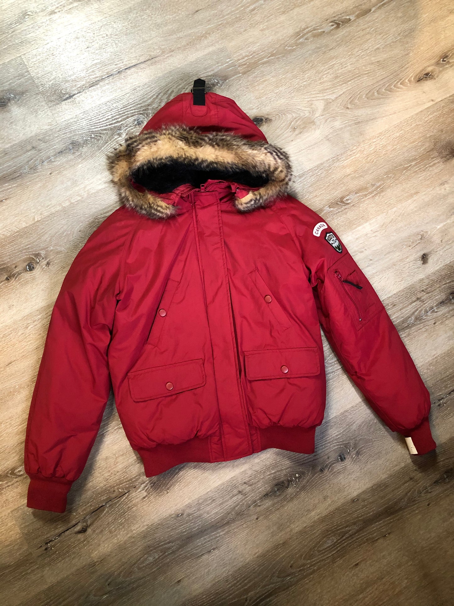 Kingspier Vintage - Roots down-filled bomber jacket in red with faux fur trimmed hood, zipper closure, flap pockets and slash pockets, “Stay Warm Eh” written on the inside pocket. Size medium.