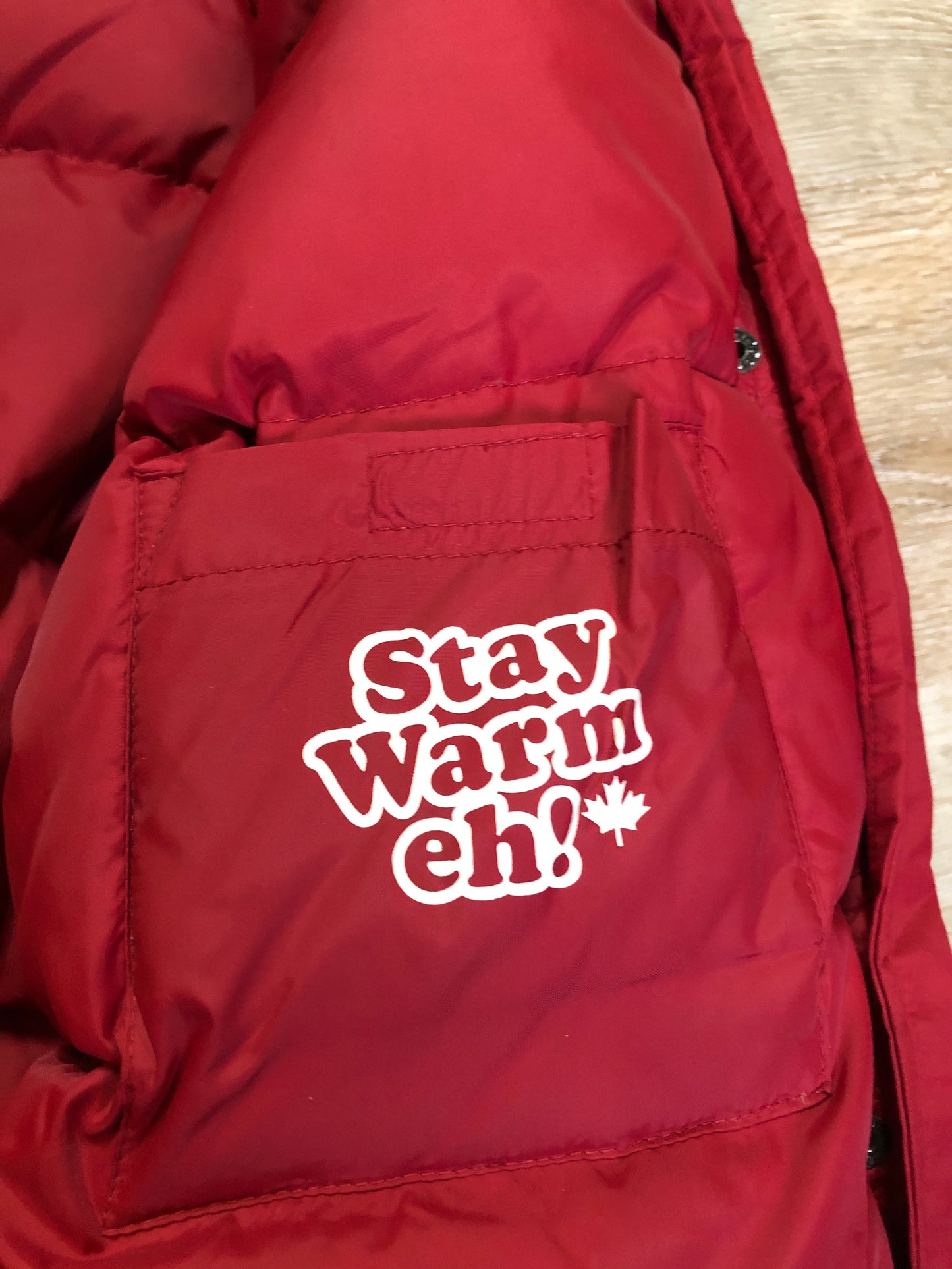 Kingspier Vintage - Roots down-filled bomber jacket in red with faux fur trimmed hood, zipper closure, flap pockets and slash pockets, “Stay Warm Eh” written on the inside pocket. Size medium.