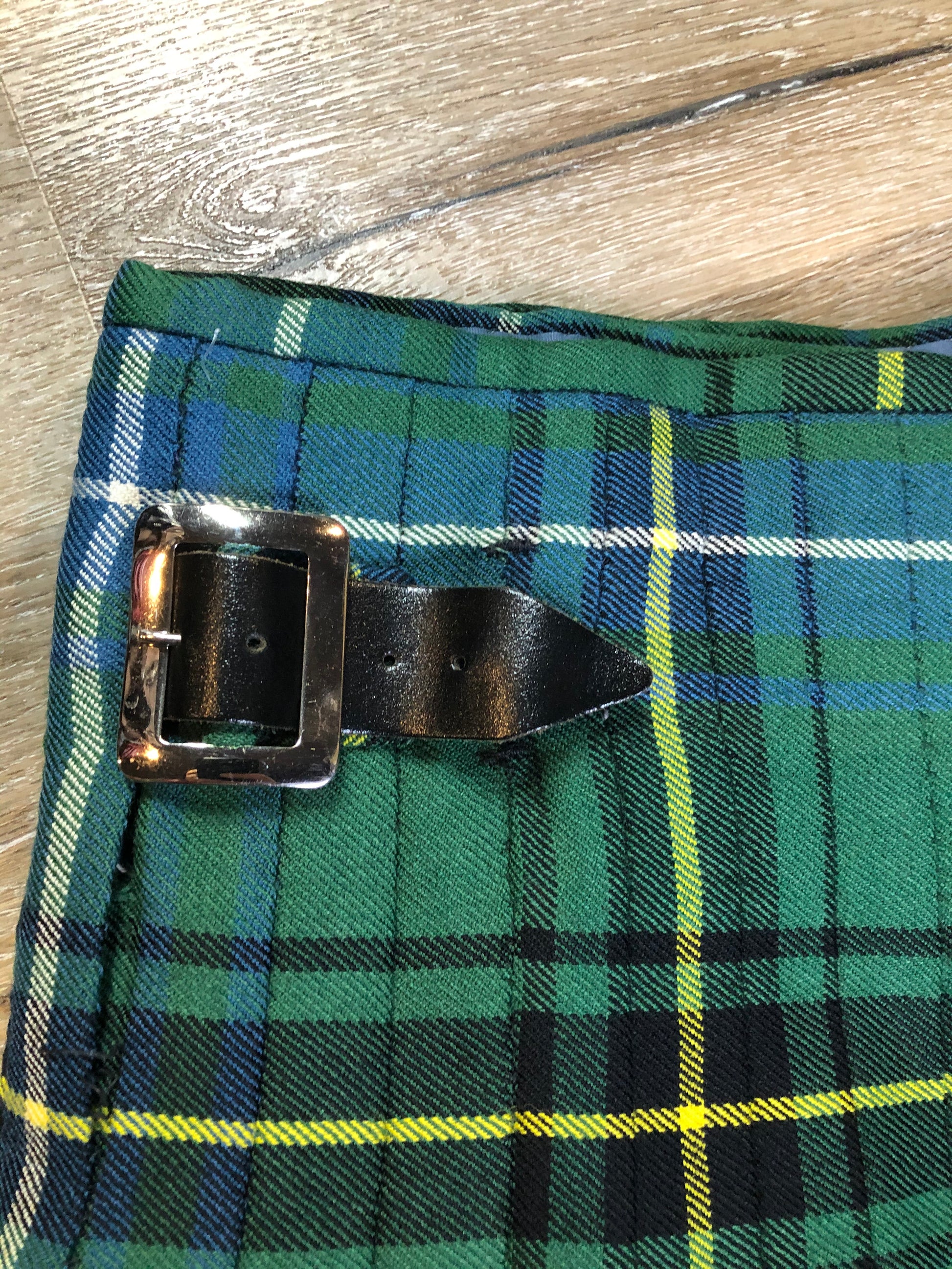 Kingspier Vintage - Green, blue, black, yellow and white plaid/ tartan kilt with leather straps on each side to adjust size. Kilt is partially lined on the inside. Fibres unknown.