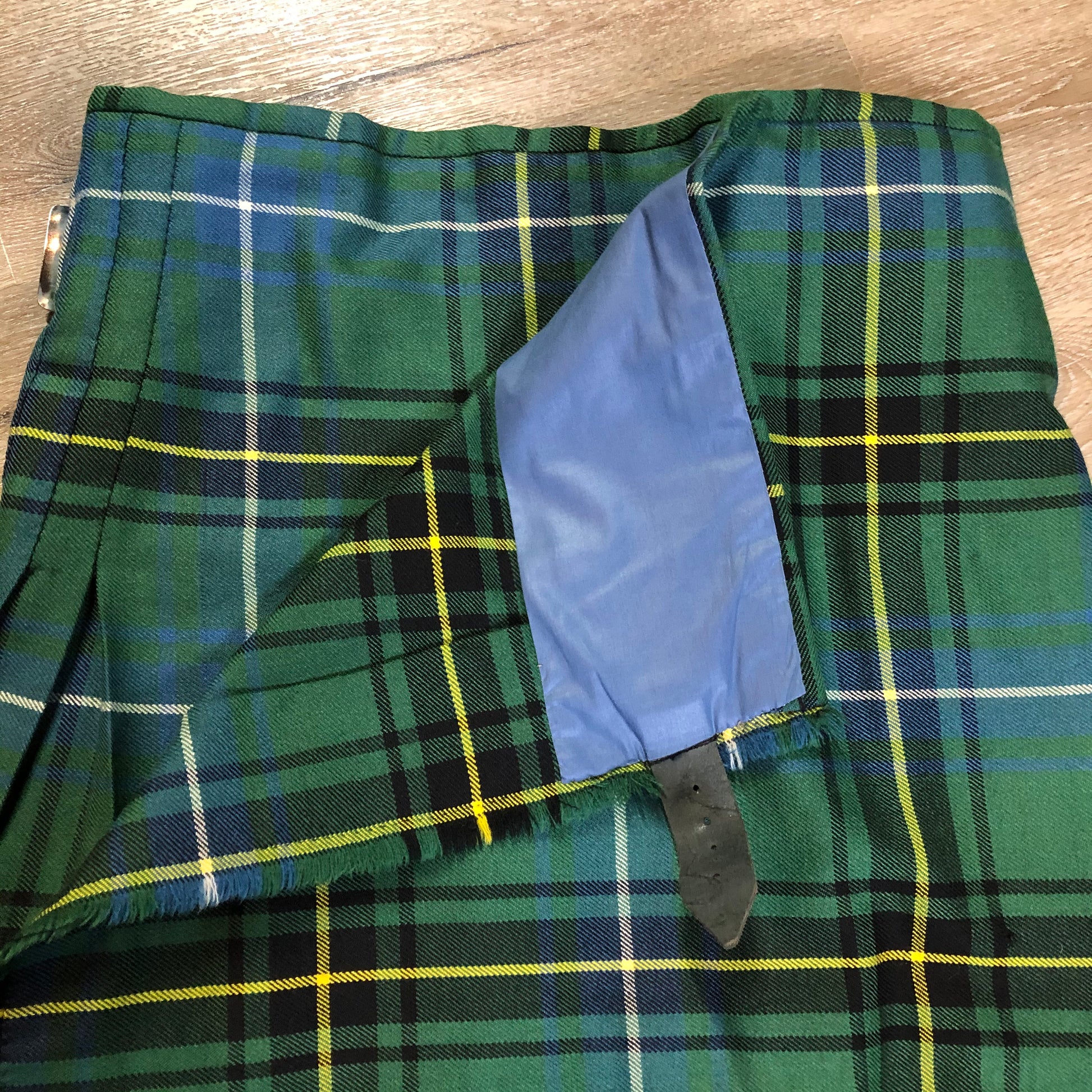 Kingspier Vintage - Green, blue, black, yellow and white plaid/ tartan kilt with leather straps on each side to adjust size. Kilt is partially lined on the inside. Fibres unknown.