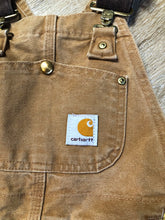 Load image into Gallery viewer, Kingspier Vintage - Kids Carhartt Sleeveless cotton canvas overalls in tan brown with Carhartt logo. Overalls feature adjustable shoulder straps with buckle fastening, patch pocket in the chest and pockets in the front and back, overalls button at the waist and have reinforced knees. Size childs medium.
