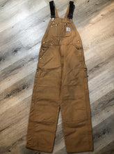 Load image into Gallery viewer, Kingspier Vintage - Carhartt Sleeveless duck canvas overalls in tan brown with Carhartt logo. Overalls feature adjustable shoulder straps with buckle fastening, hammer loop, patch pocket on the chest, side utility pockets, pockets in the front and back, overalls button at the waist and have reinforced knees. Size 32X30.
