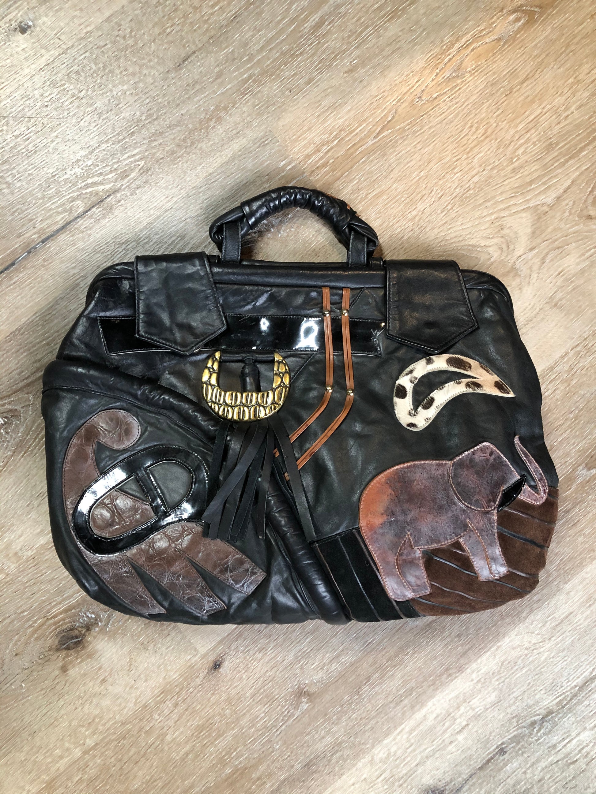 Kingspier Vintage - Upcycled leather bag with top handle, loops to attach a longer strap. (strap not included), snap closures, dinosaur and wooly mammoth design, a tassel and some other unique leather details.

Length - 18”
Width - 4”
Height - 13”

This bag is in great condition with some minor wear.