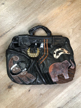 Load image into Gallery viewer, Kingspier Vintage - Upcycled leather bag with top handle, loops to attach a longer strap. (strap not included), snap closures, dinosaur and wooly mammoth design, a tassel and some other unique leather details.

Length - 18”
Width - 4”
Height - 13”

This bag is in great condition with some minor wear.

