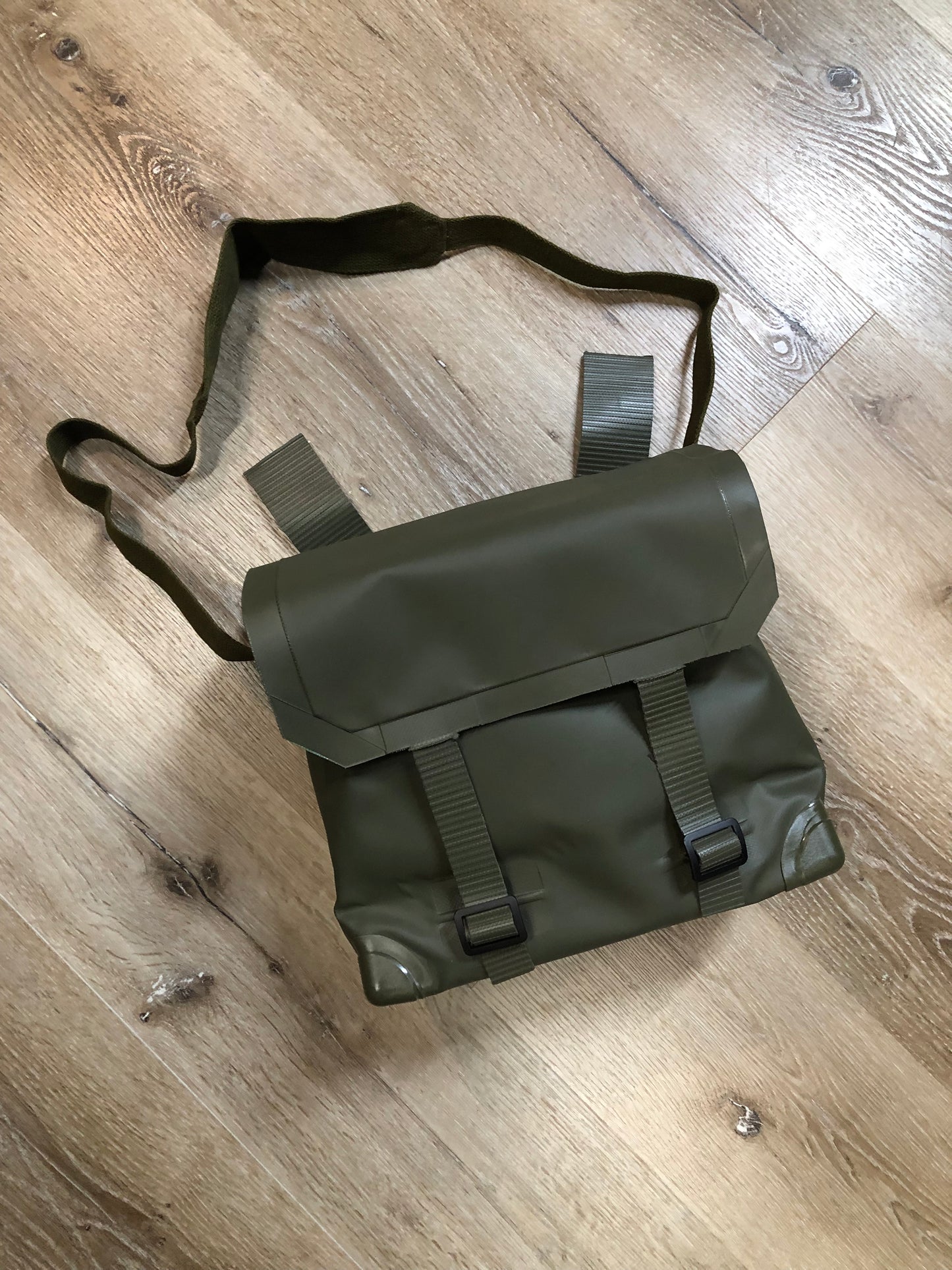 Kingspier Vintage - Deadstock Dutch military issue shoulder bag in dark olive made with waterproof PVC. This bag features a divided main compartment with protective inside flaps that ties in the center and an adjustable canvas shoulder strap.